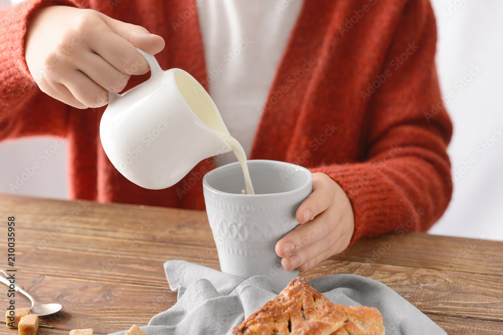 女人把牛奶倒进桌子上的一杯茶里