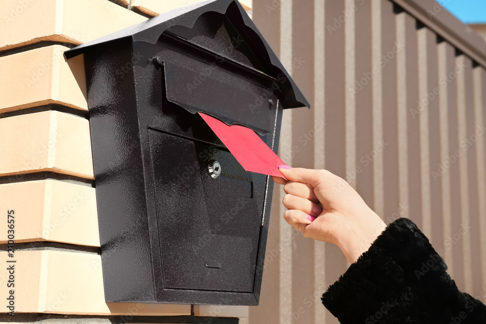 Woman putting letter in mailbox outdoors