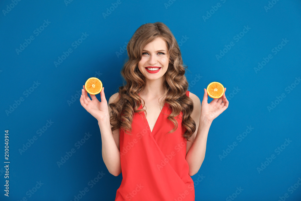 Beautiful young woman with halves of orange on color background