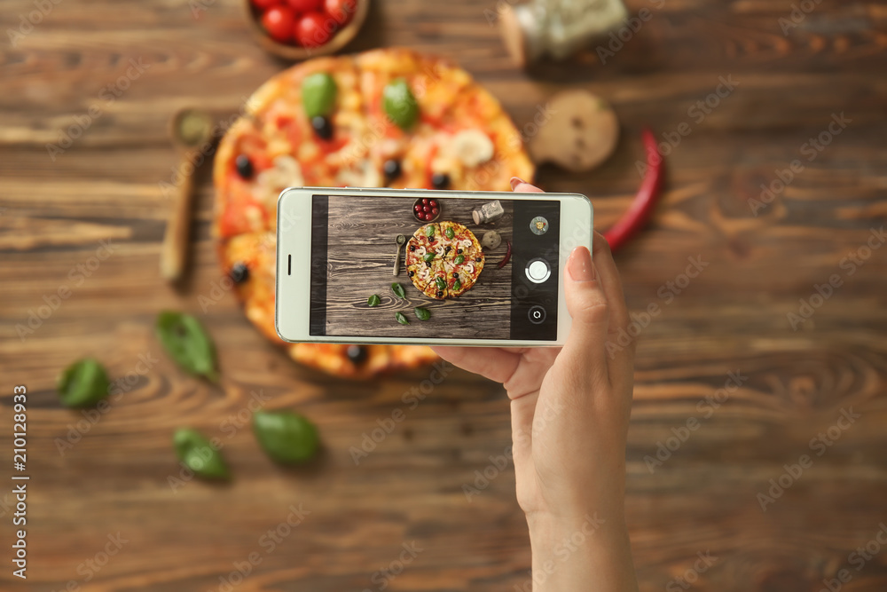 Woman taking photo of delicious Italian pizza with mobile phone