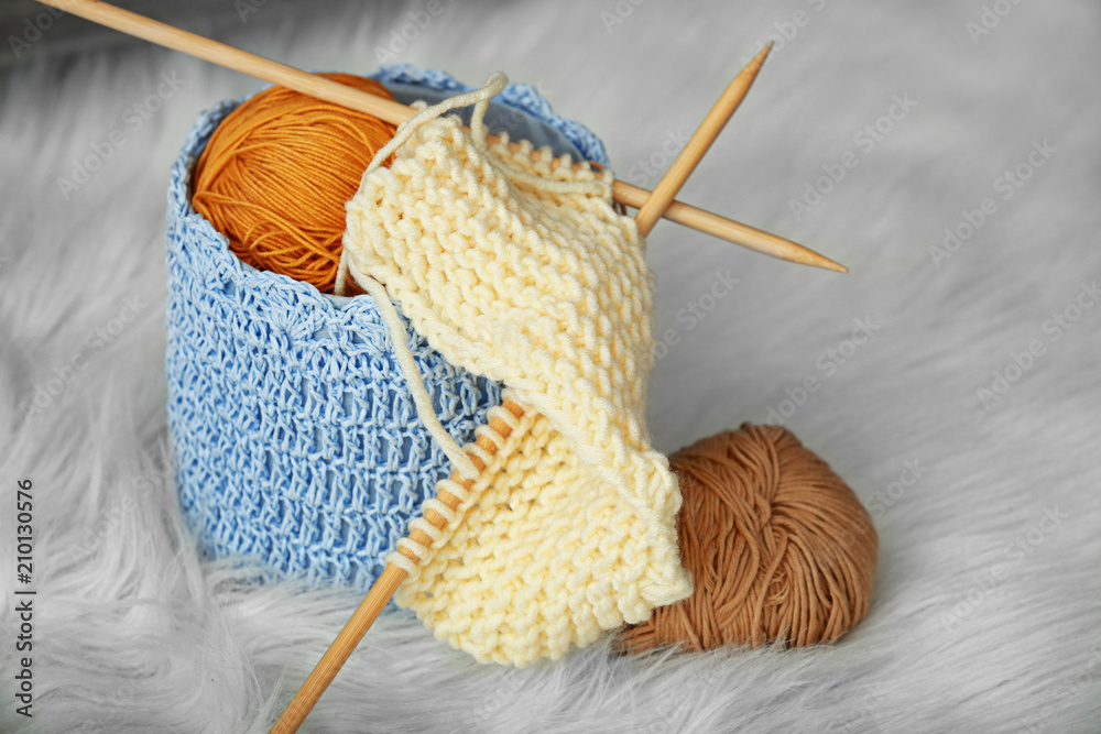 Basket with knitting yarn and unfinished clothes on fluffy carpet