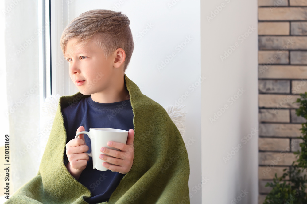 可爱的小男孩在窗户附近拿着一杯热可可饮料