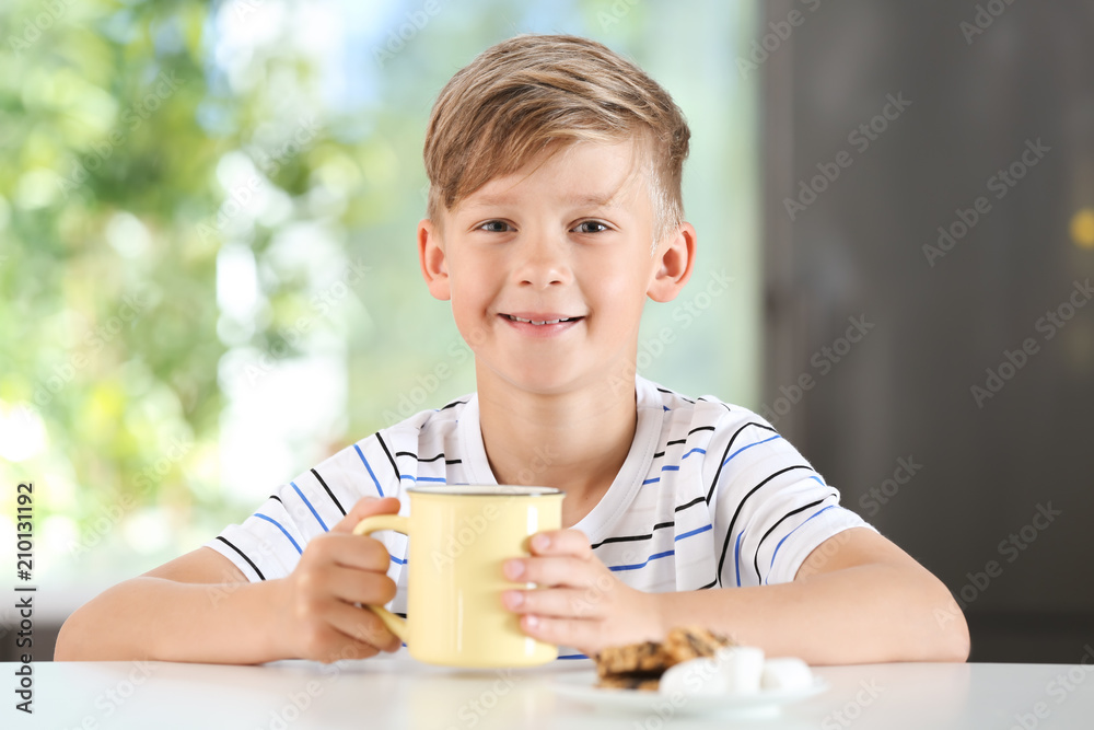 Cute little boy with cup of hot cocoa drink at table