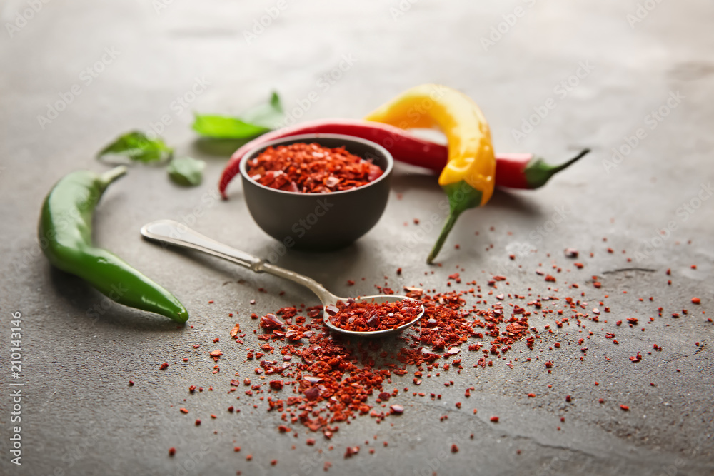 Spoon and bowl with granulated chili pepper on light background