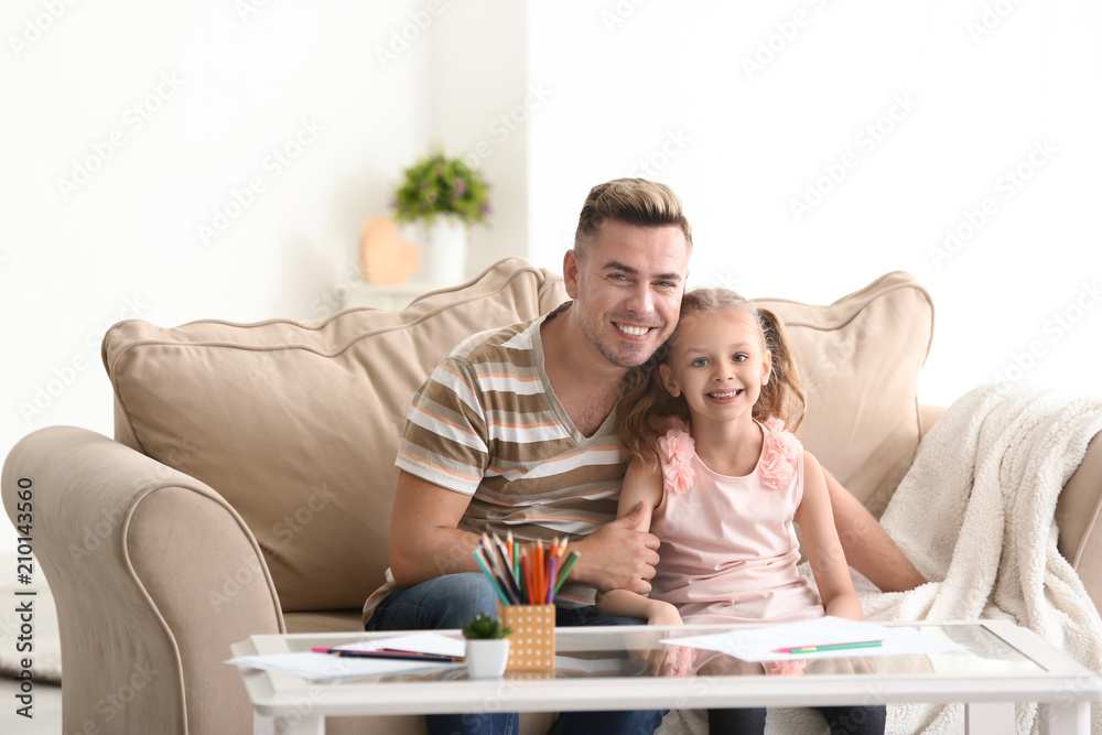 Happy father and daughter sitting on sofa at home