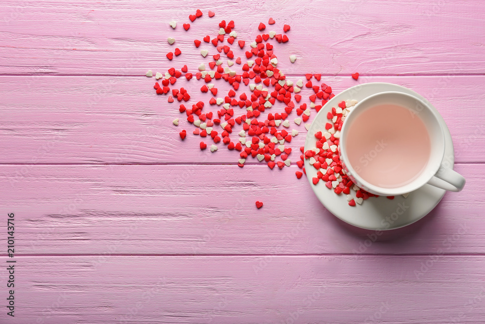 Heart-shaped candies and cup of beverage on wooden background