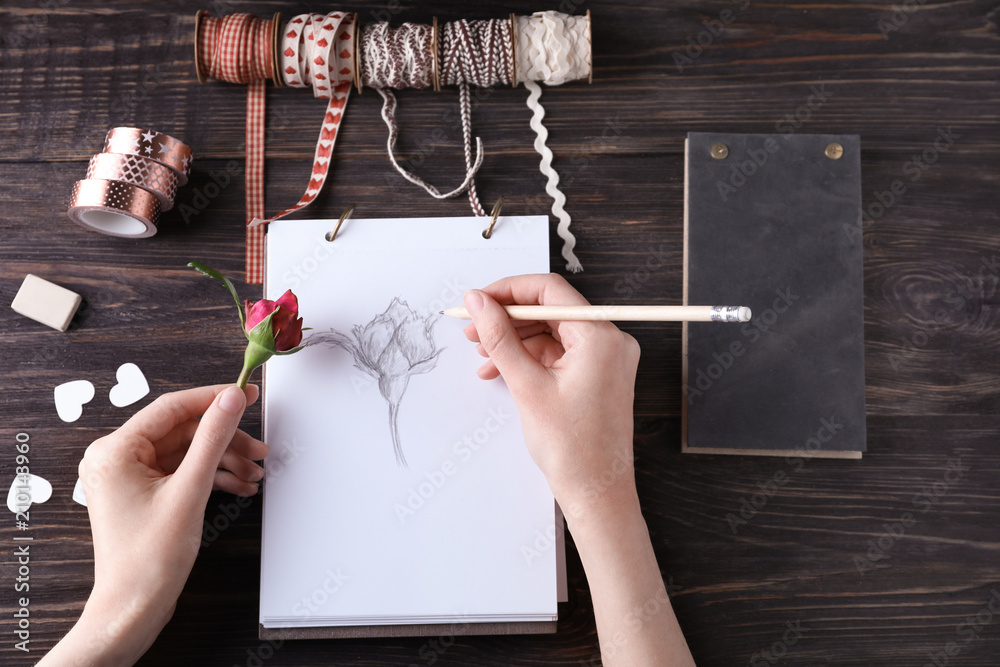 Woman drawing beautiful rose on sketch pad