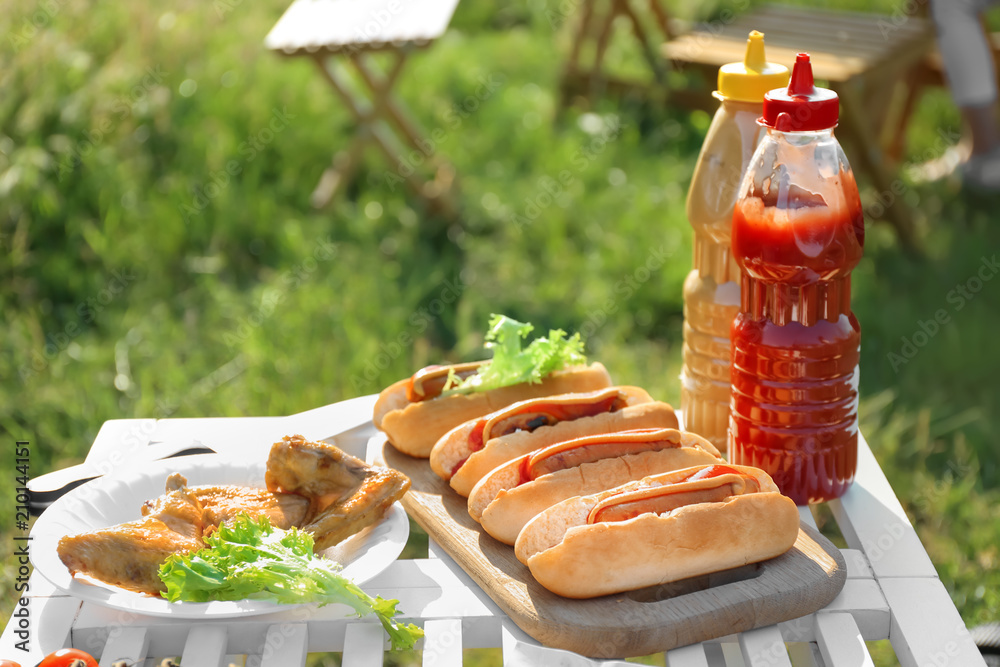 户外餐桌上美味的热狗和烤鸡翅。夏季野餐