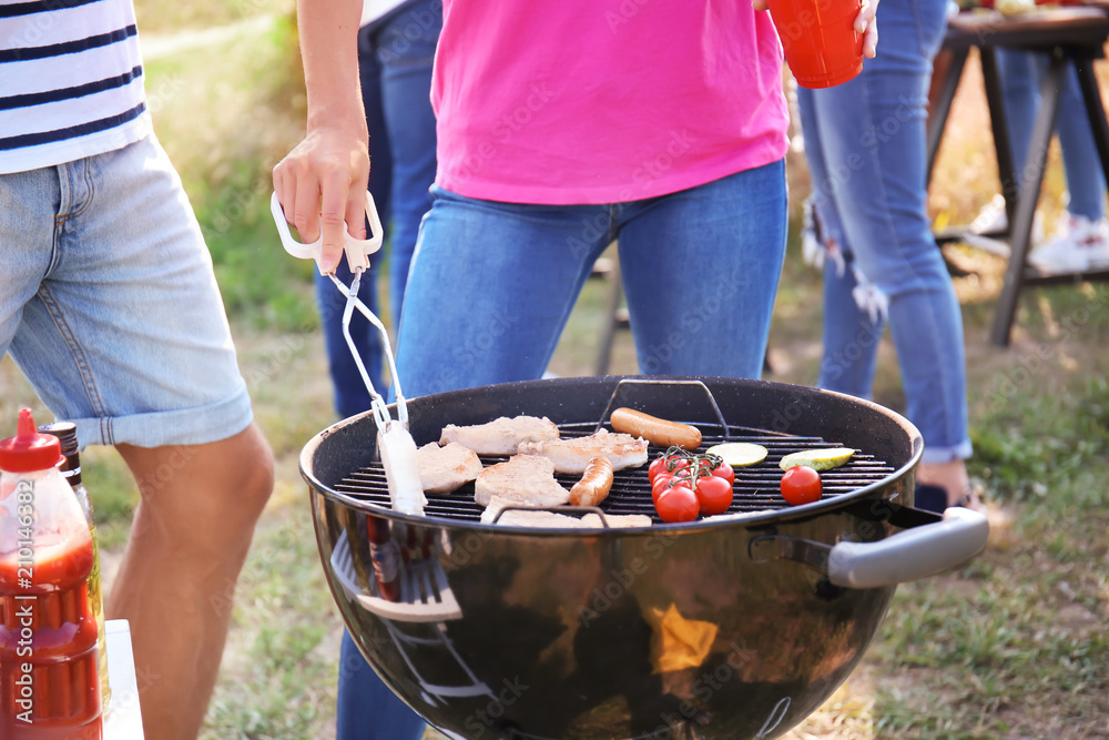 People preparing meat and vegetables on modern grill outdoors