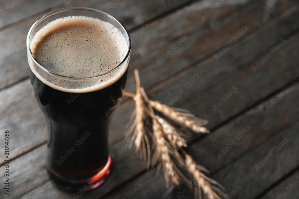 Glass with cold beer and spikelets on wooden background