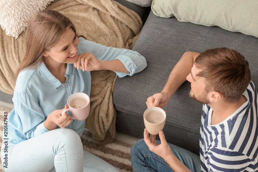 Happy young couple drinking hot coffee while resting at home