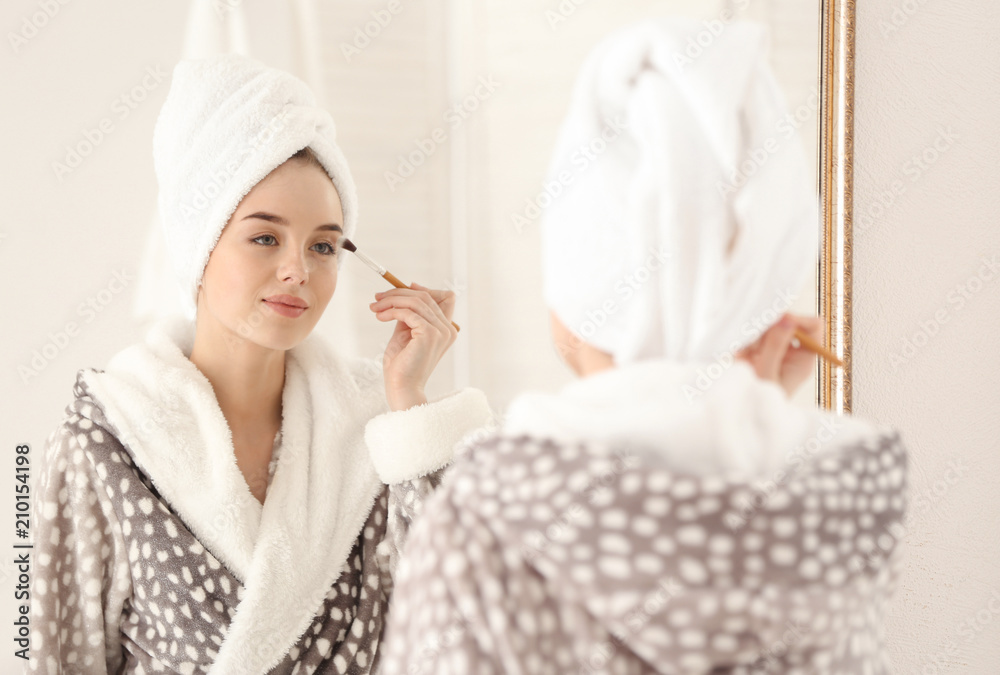 Beautiful young woman applying makeup in morning