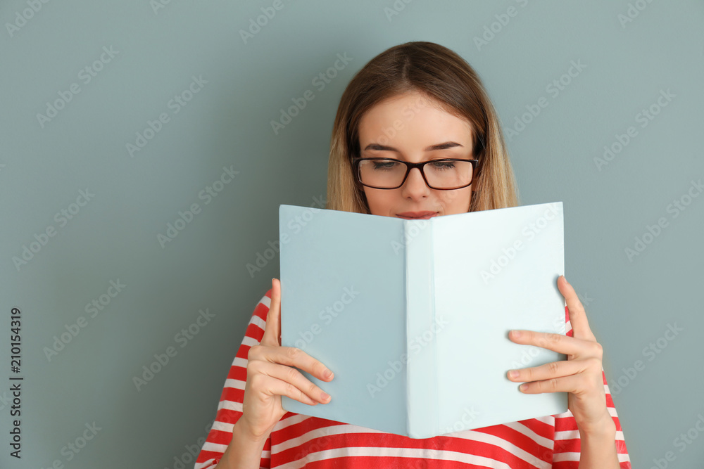 Young woman reading book on color background