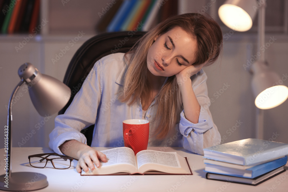 Young woman reading book at table in evening