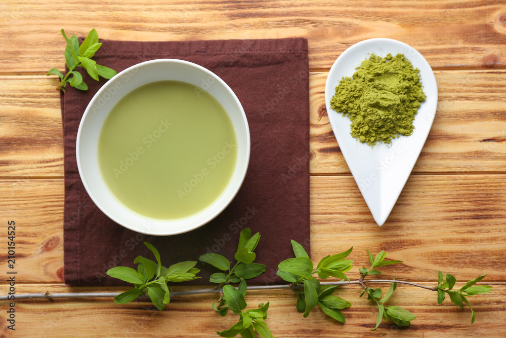 Bowl of fresh matcha tea and plate with powder on table