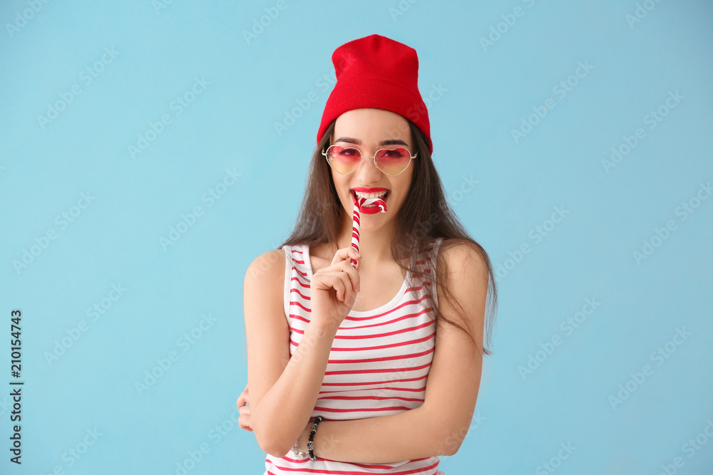 Attractive young woman with candy cane on color background