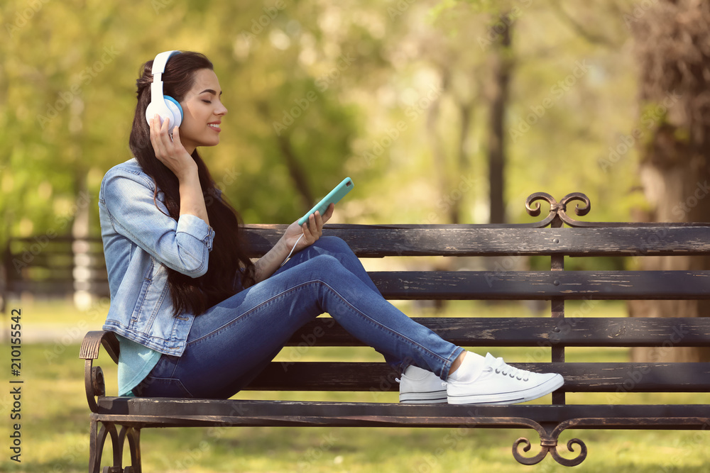 Beautiful young woman listening to music while resting in park