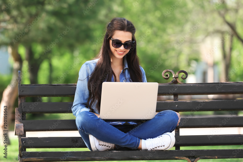 Beautiful young woman resting in park with laptop