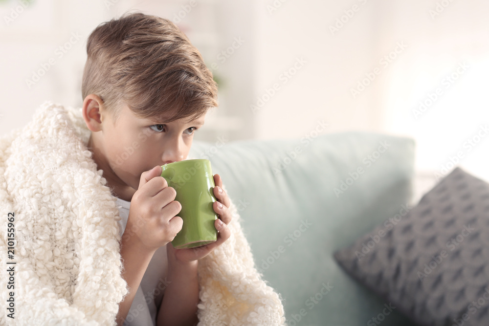 Cute little boy with cup of hot cocoa drink on sitting sofa at home