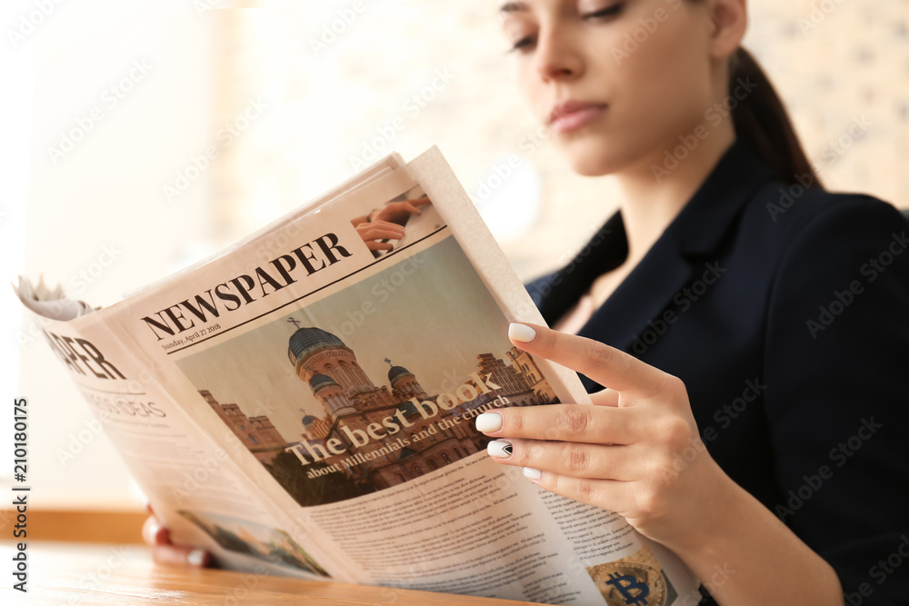 Young businesswoman reading newspaper in office