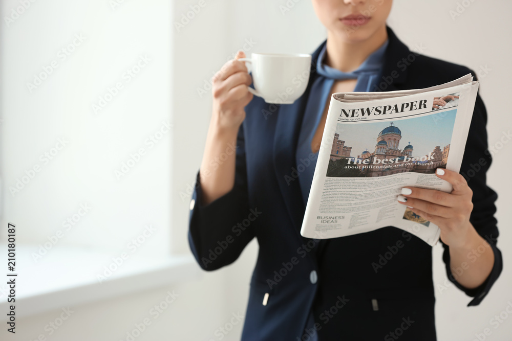 Young woman reading newspaper while drinking coffee in office