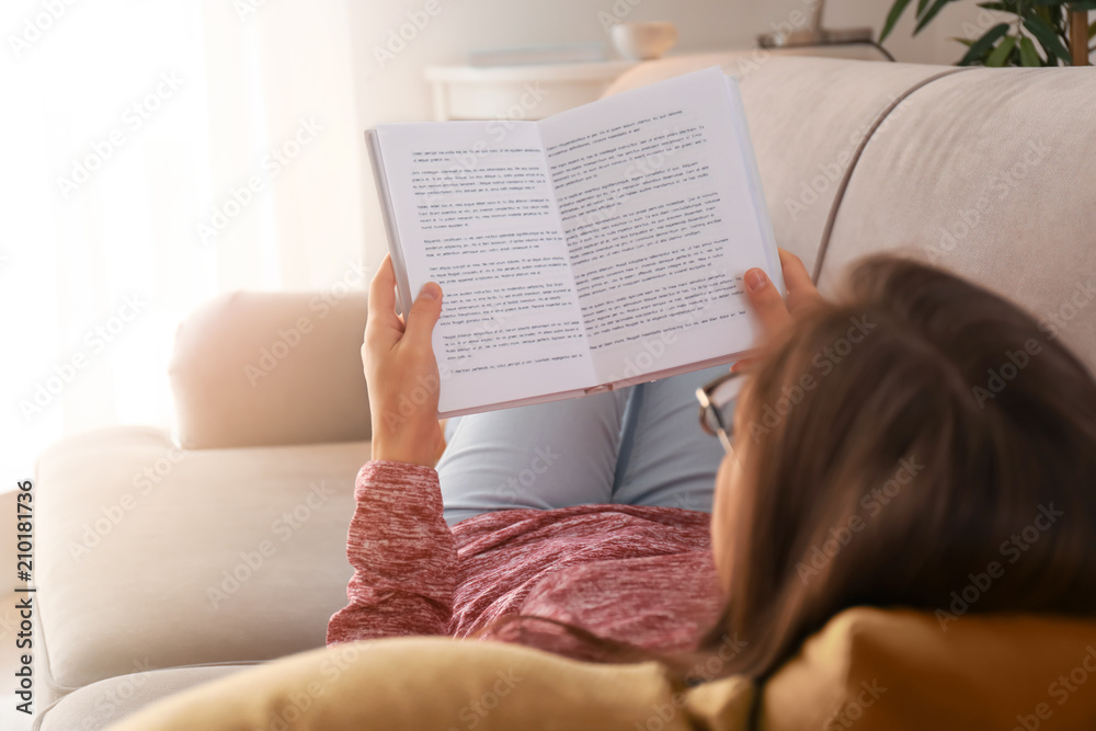 Young woman reading book on sofa at home