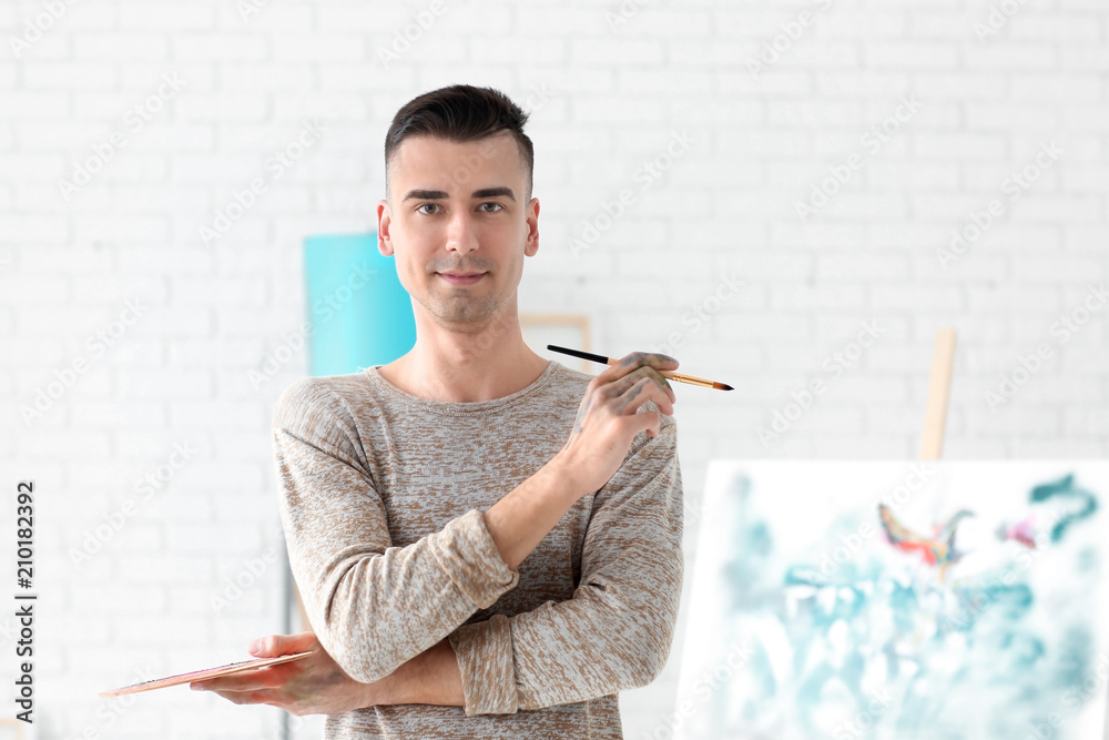 Male artist with paintbrush and palette in workshop