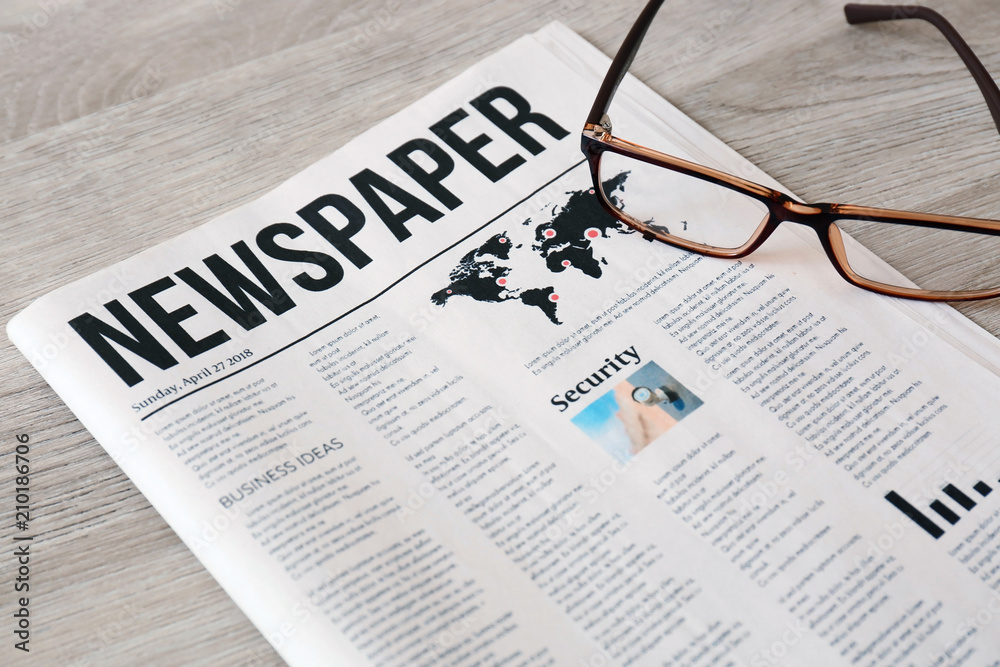 Newspaper with glasses on wooden background