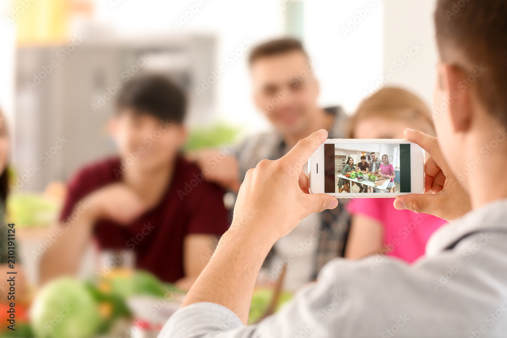 Young man taking photo of his friends in kitchen