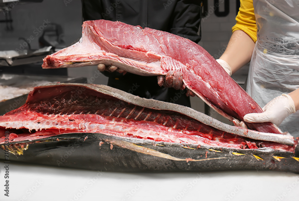 Men working with fresh tuna at table in fish market