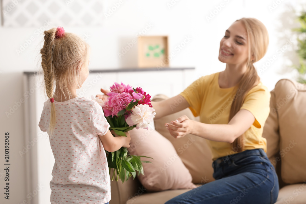 Cute little girl giving flowers to her mother at home