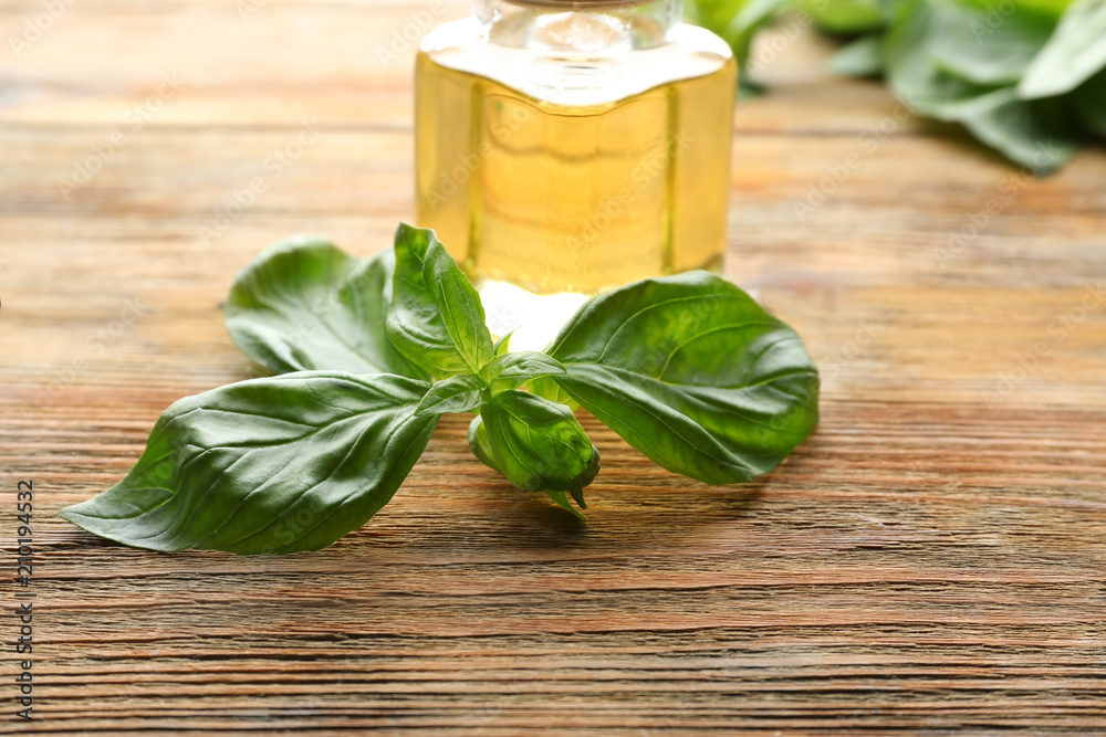 Jar of oil with fresh basil on wooden table