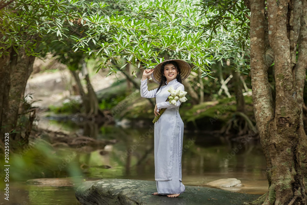 美丽的女人戴着帽子，穿着敖黛传统的越南连衣裙站在森林里。