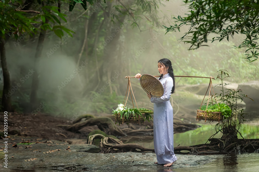 美丽的女人戴着帽子，穿着敖黛传统的越南连衣裙站在森林里。