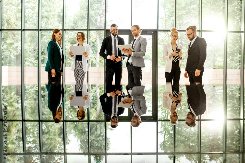 Business people standing with gadgets at the modern office hall with window on the background overlo