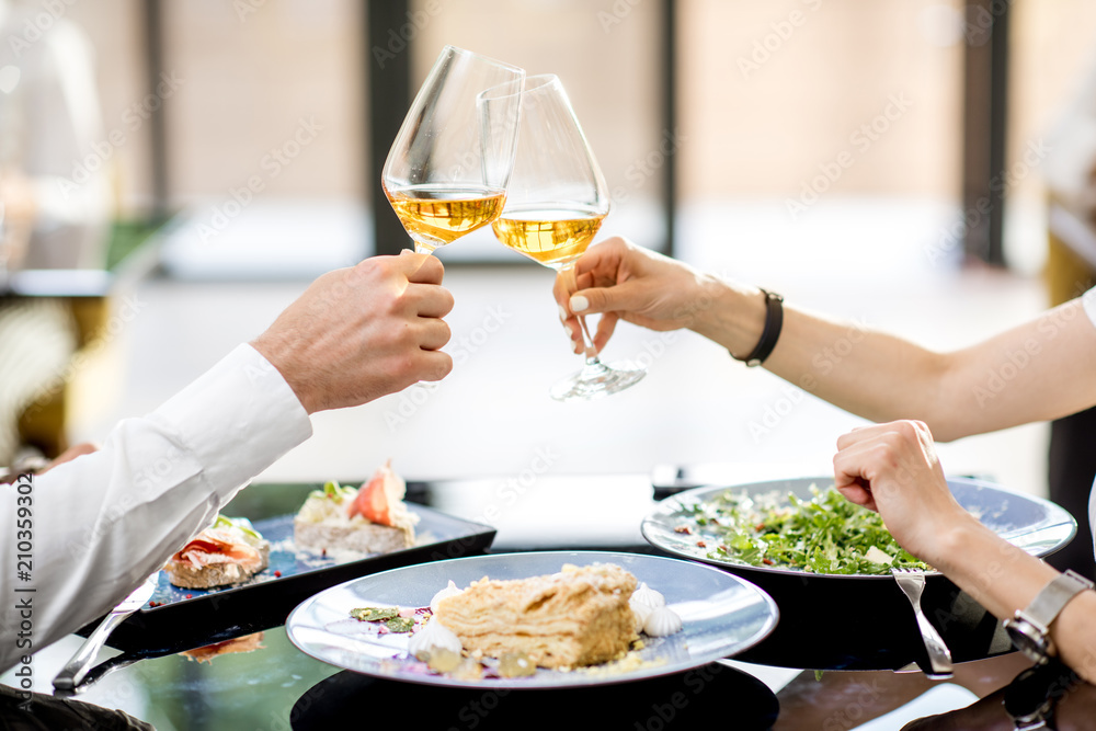 Clinking with wine glasses during a business lunch at the restaurant, close-up view