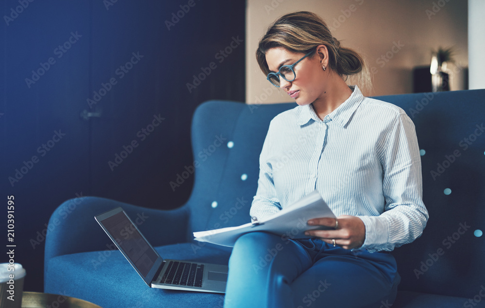 Focused young businesswoman sitting on a couch going through documents