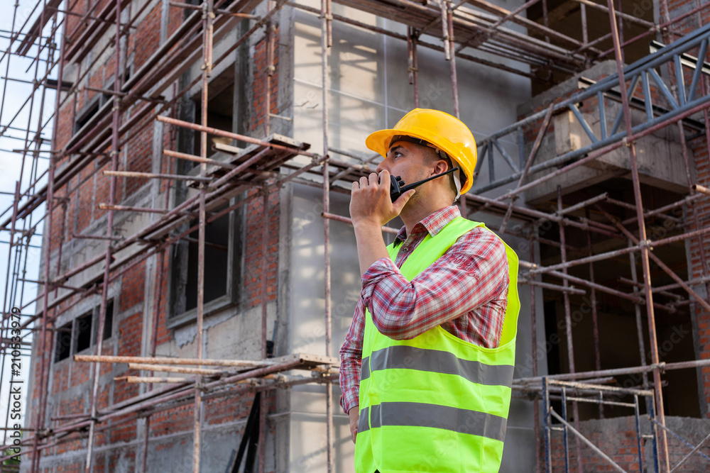 建筑工程师在建筑工地前工作时使用对讲机与助手交谈。