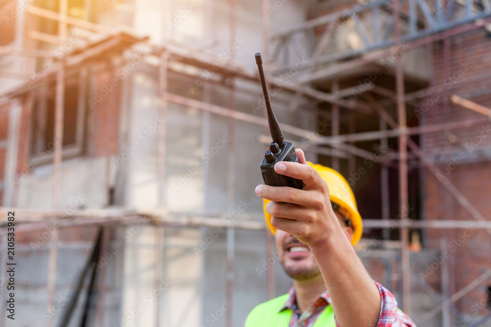 Architect engineer using walkie-talkie talking with assistant while working front of building site.