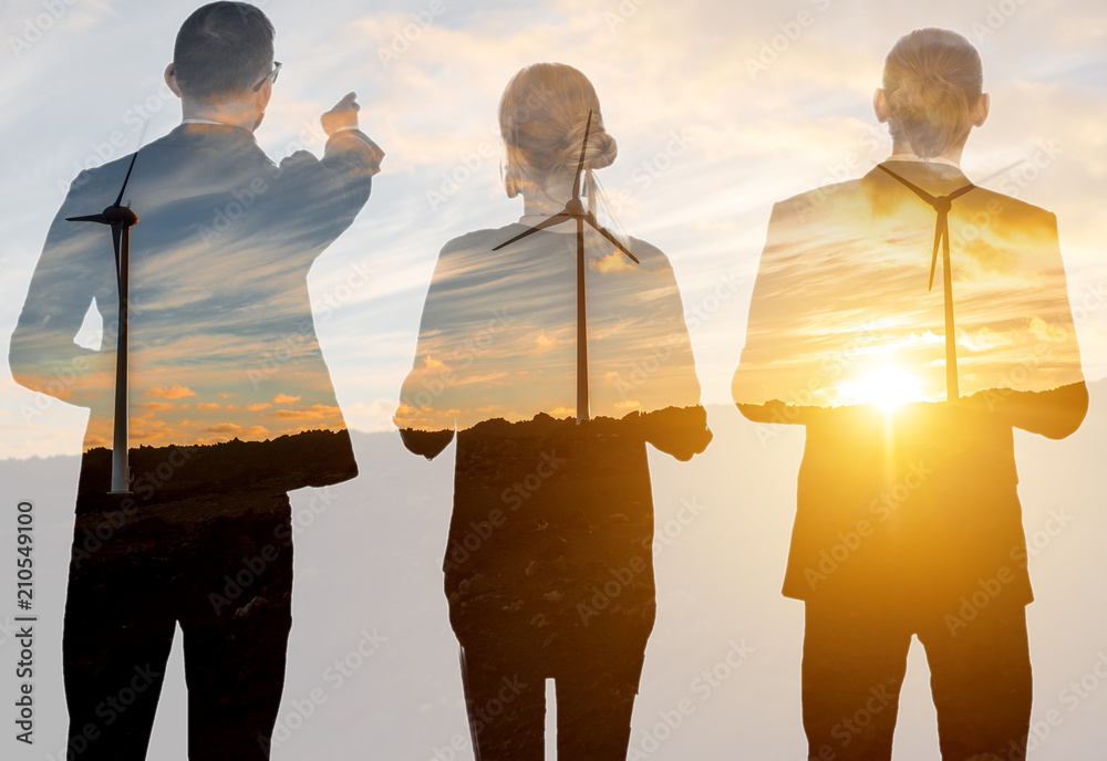 Silhouettes of business people standing back on the landscape background with wind turbines during t