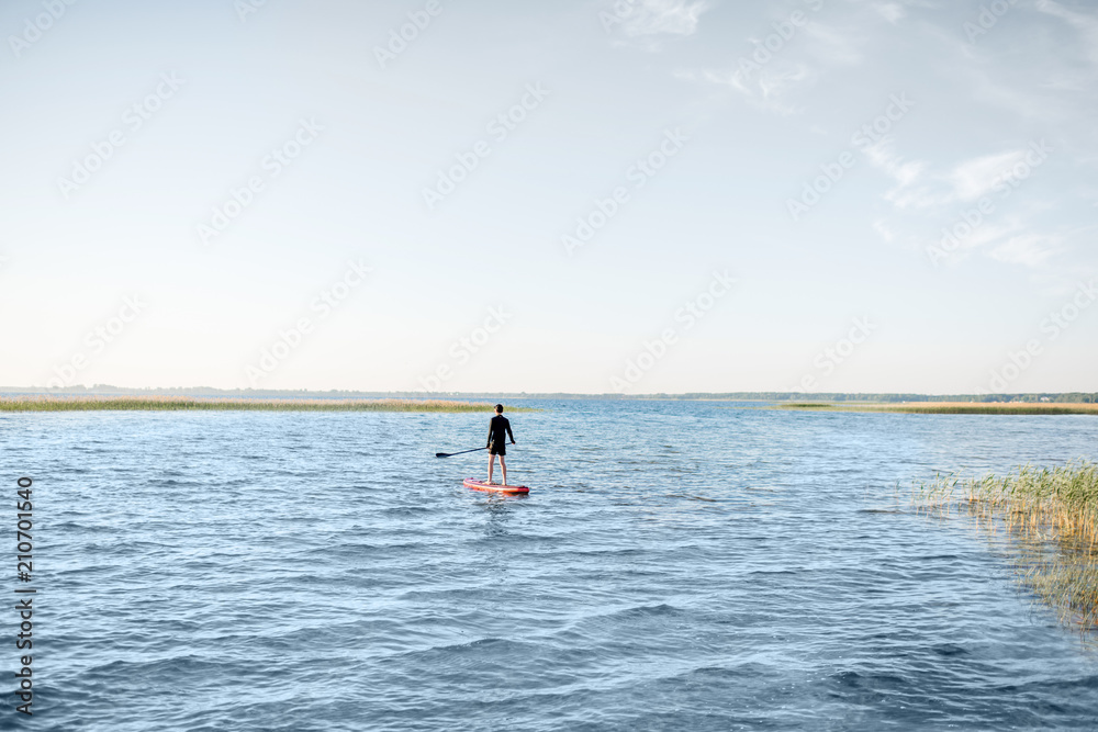 Man paddleboarding on the lake during the morning light, wide landscape view with blue water and sky