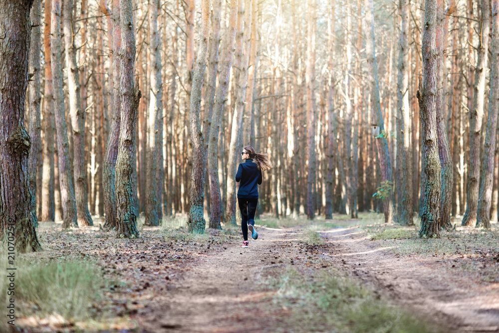 穿着黑色运动服的女人早上在松林里跑步，视野开阔