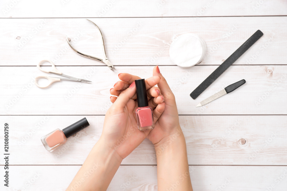 Female hands applying purple nail polish on wooden table with towel and nail set