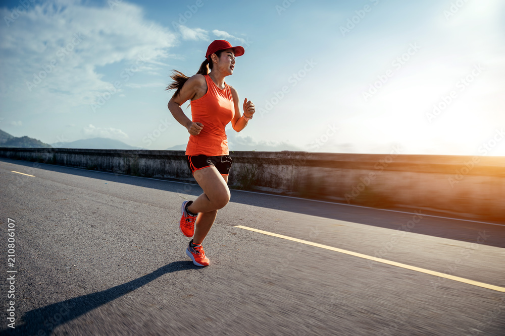 An asian woman athletic is jogging on the concrete road, she is warming her body and tideten her tyi