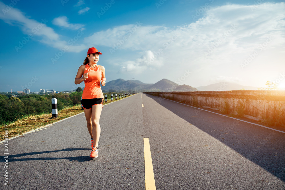 An asian woman athletic is jogging on the concrete road, she is warming her body and tideten her tyi