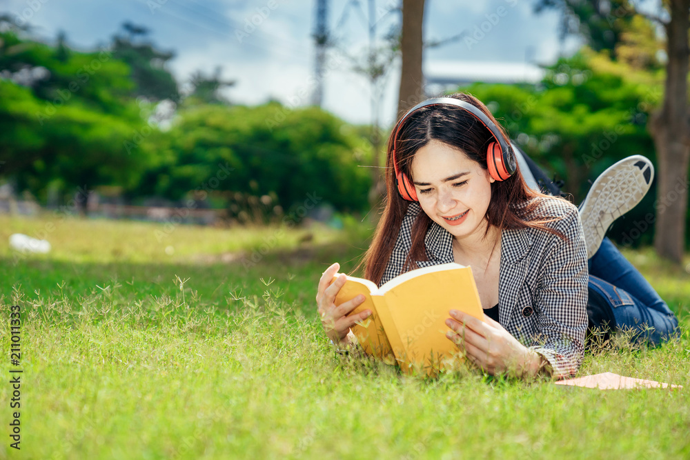 A young teenage student in university smiling and reading the book in summer holiday. She listening 