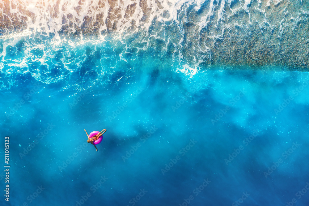 Aerial view of woman swimming on the pink swim ring in the transparent sea and beautiful waves in Eu