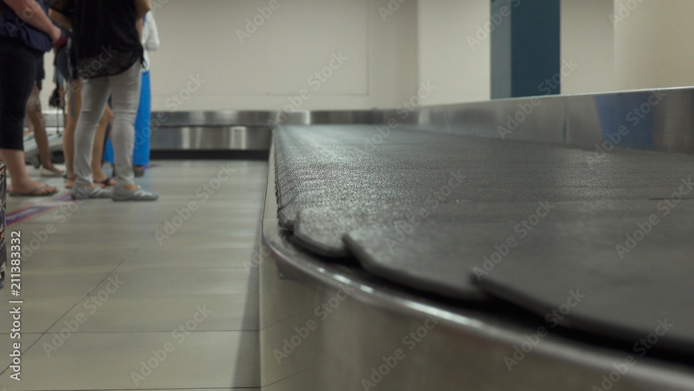 CLOSE UP Unrecognizable people waiting to claim their bags next to luggage belt