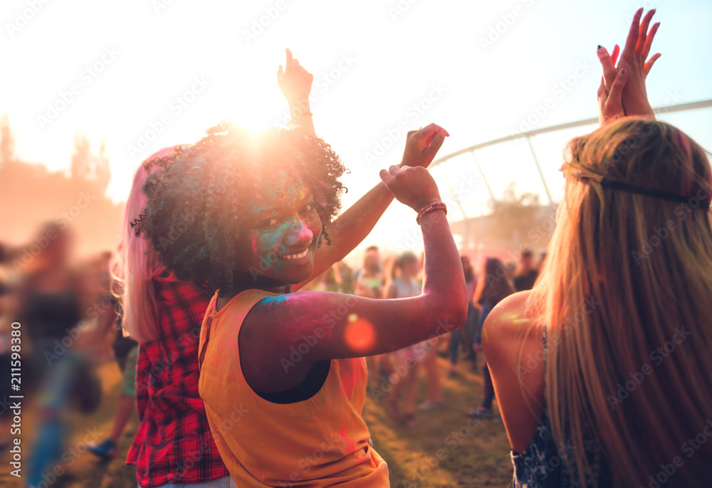 Multiethnic girls covered in colorful powder dancing and celebrating summer holi festival