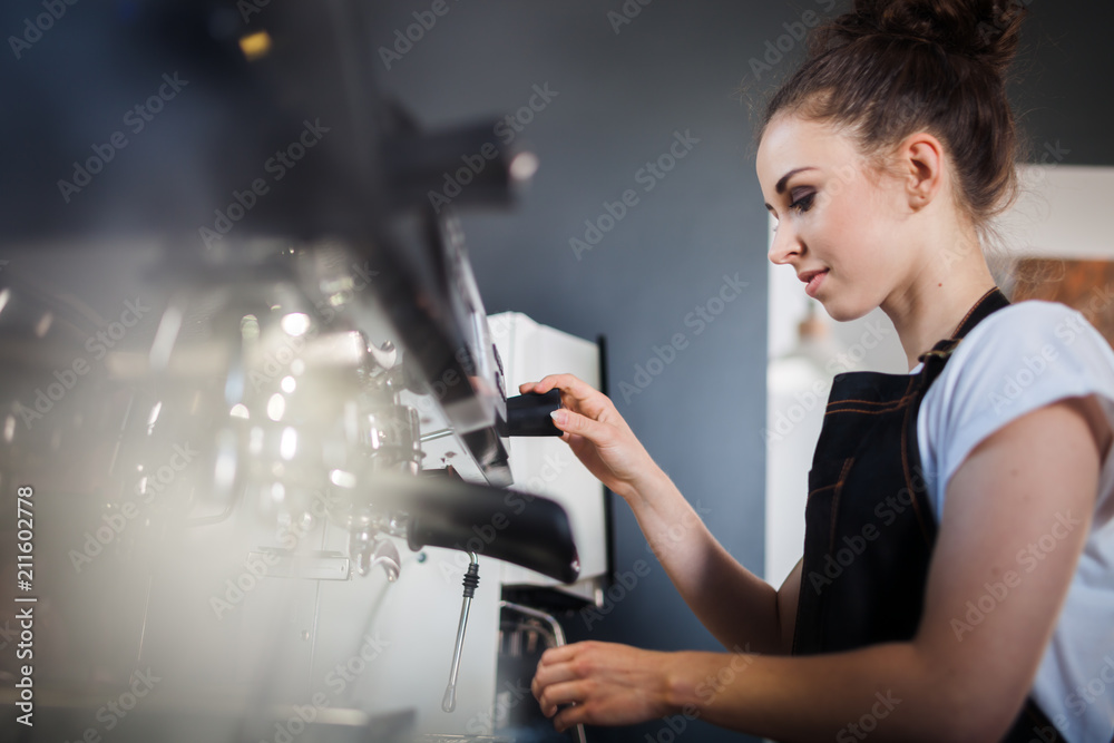 Young woman barista preparing coffee using machine in the cafe